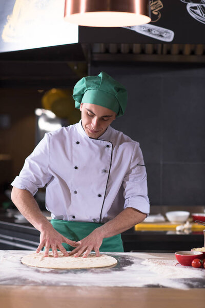 Chef preparing dough for pizza rolling with hands on sprinkled with flour table