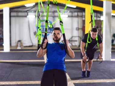 Spor yapan iki genç sporcu spor salonunda jimnastik yüzükleriyle barfiks çekiyorlar.