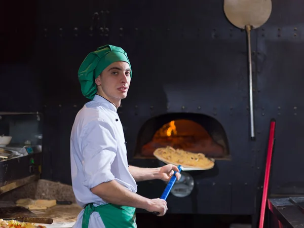 Шеф-повар кладет вкусную пиццу в печь из кирпича — стоковое фото