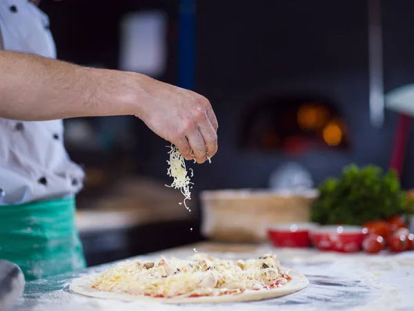 Chef espolvorear queso sobre masa de pizza fresca —  Fotos de Stock