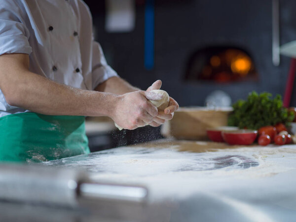 Chef hands preparing dough for pizza on table sprinkled with flour closeup