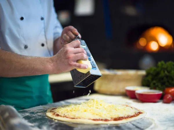 Chef espolvorear queso sobre masa de pizza fresca —  Fotos de Stock