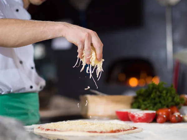 Chef streut Käse über frischen Pizzateig — Stockfoto