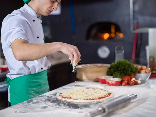 Chef Streut Käse Über Frischen Pizzateig Auf Küchentisch — Stockfoto