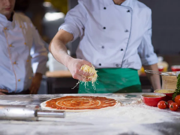 Chef Streut Käse Über Frischen Pizzateig Auf Küchentisch — Stockfoto