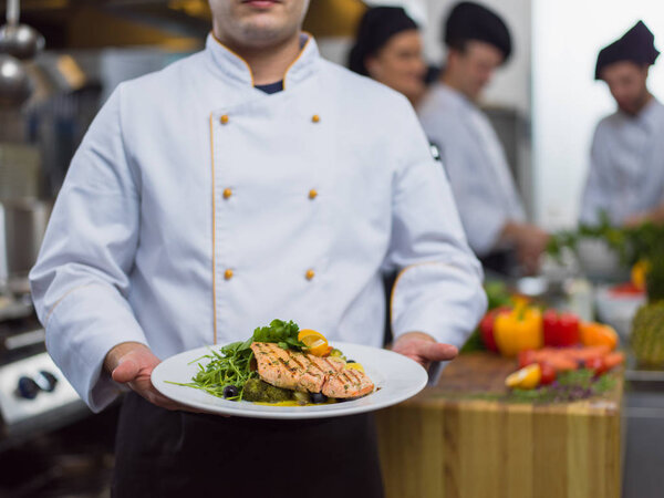Chef holding fried Salmon fish fillet with vegetables for dinner in a restaurant kitchen