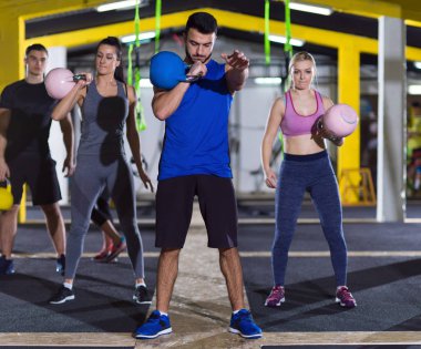 Çapraz fitness stüdyosunda kettlebell egzersizleri yapan bir grup sağlıklı genç sporcu.