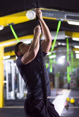 Genç kaslı adam çapraz fitness salonunda ip tırmanışı yapıyor.