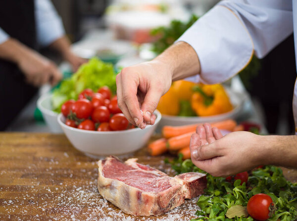 Chef putting salt on juicy slice of raw steak