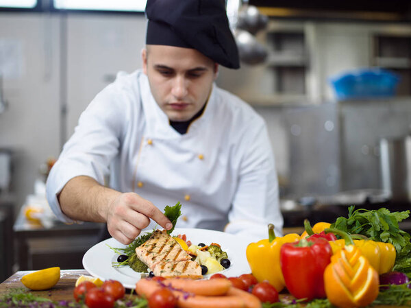 Cook chef decorating garnishing prepared meal dish on the plate in restaurant commercial kitchen
