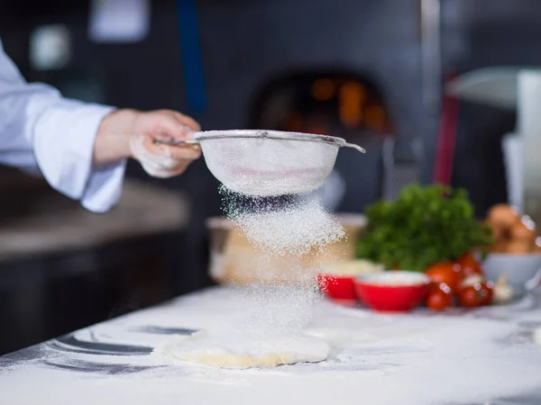 Szef kuchni posypywanie mąki na świeże ciasto pizzy — Zdjęcie stockowe