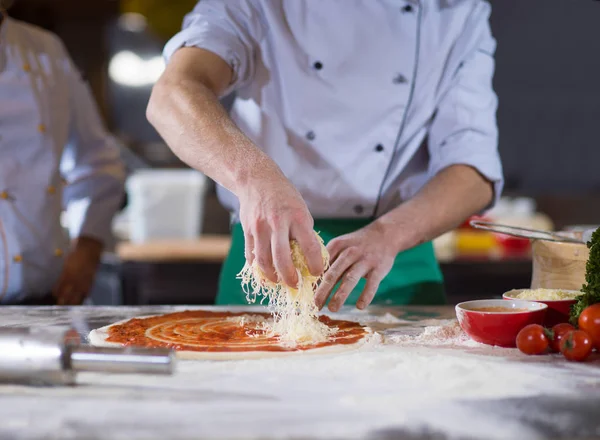 Chef espolvorear queso sobre masa de pizza fresca —  Fotos de Stock