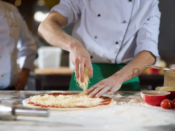 Chef streut Käse über frischen Pizzateig — Stockfoto