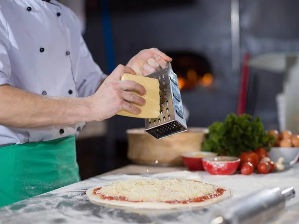 Chef streut Käse über frischen Pizzateig — Stockfoto