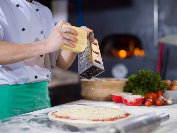 Chef polvilhando queijo sobre massa de pizza fresca — Fotografia de Stock
