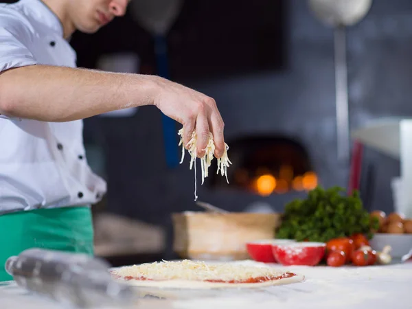 Chef spolverare formaggio sopra pasta fresca pizza — Foto Stock