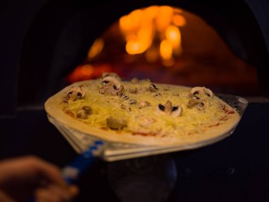 Şef lezzetli pizzayı tuğla fırına koyuyor.