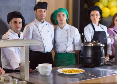 Ekip şefleri mutfakta restoran müdürüne lezzetli yemekler sunuyor.