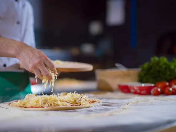 Chef espolvorear queso sobre masa de pizza fresca —  Fotos de Stock