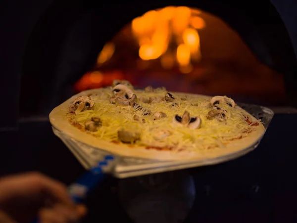 Chef colocando deliciosa pizza para forno de madeira de tijolo — Fotografia de Stock