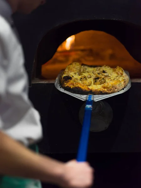 Шеф-повар удаляет горячую пиццу из плиты — стоковое фото