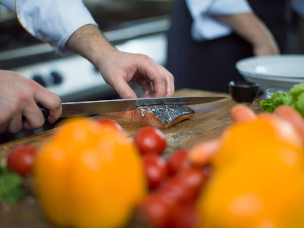 Chef hands preparing marinated Salmon fish fillet for frying in a restaurant kitchen