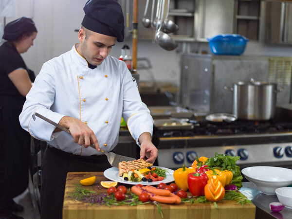 Cook chef decorating garnishing prepared meal dish on the plate in restaurant commercial kitchen