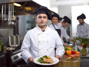 Şef, restoran mutfağında sebzeli kızarmış somon balığı filetosu tutuyor.