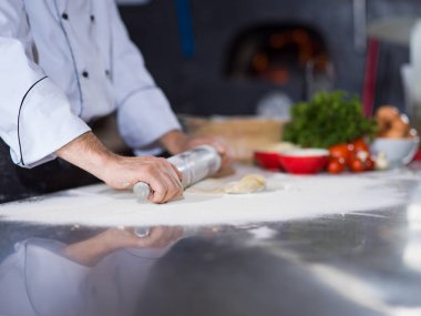 Şef pizza hamuru hazırlıyor. Üzerinde un tokası serpiştirilmiş.