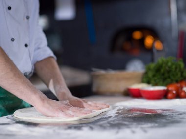 Şef pizza için hamur hazırlıyor. Elleri un serpiştirilmiş.