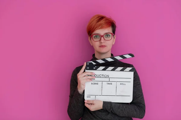 红头发女人拿着粉色背景的电影拍子 — 图库照片