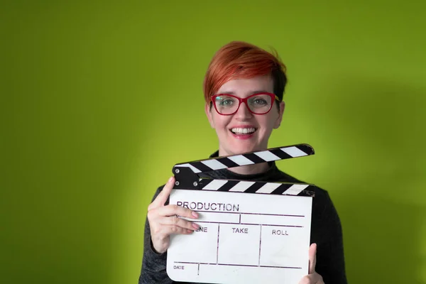 Kızıl saçlı kadın yeşil arka planda film alkışını tutuyor. — Stok fotoğraf