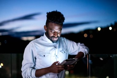 Geceleri sokakta tablet bilgisayar kullanan genç bir afro adam.