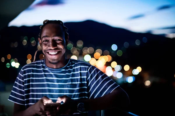 Jovem afro homem na rua à noite usando telefone — Fotografia de Stock