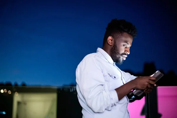 Jeune homme afro dans la rue la nuit à l'aide d'un ordinateur tablette — Photo