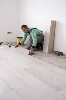 Seramik ahşap efekt fayanslarını döşeyen yetenekli bir işçi. İşçi, yeni apartmanın inşaat alanında döşeme kaplaması yapıyor.