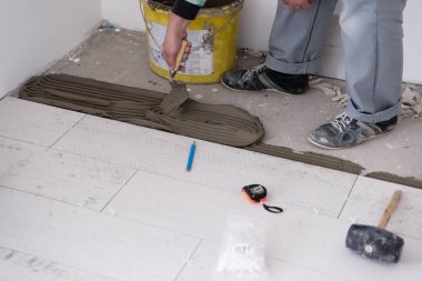 Seramik ahşap efekt fayanslarını döşeyen yetenekli bir işçi. İşçi, yeni apartmanın inşaat alanında döşeme kaplaması yapıyor.