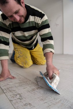 Seramik fayanslar sayılıyor. Seramik ahşap efektli fayanslar arasındaki boşluğu yeni modern dairede yerde kauçuk bir malayla dolduran dümenciler.