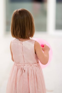 Pembe elbiseli mutlu küçük kız güzel bir akşamda evdeki pencerenin yanında balonlarla oynarken eğleniyor.