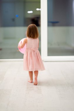 Pembe elbiseli mutlu küçük kız güzel bir akşamda evdeki pencerenin yanında balonlarla oynarken eğleniyor.