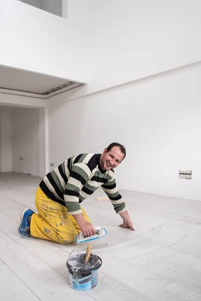 Grouting ceramic tiles. Tilers filling the space between ceramic wood effect tiles using a rubber trowel on the floor in new modern apartment