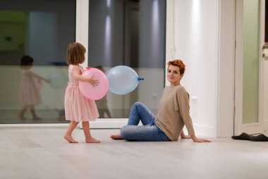 happy family spending time together young redhead mother and cute little daughter having fun while playing with balloons near the window on beautiful evening at home