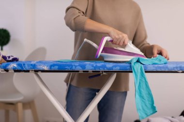 Güzel, genç, kızıl saçlı ev hanımı. Keyfi yerinde. Evde beyaz bir duvarın önündeki ütü masasında giysilerini ütülüyor.