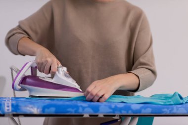 Güzel, genç, kızıl saçlı ev hanımı. Keyfi yerinde. Evde beyaz bir duvarın önündeki ütü masasında giysilerini ütülüyor.