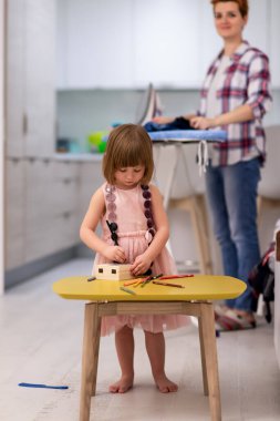 Mutlu bir aile, evde pembe elbiseli şirin bir kızla vakit geçirirken mücevher kutusunu boyar ve oynar. Bu arada genç kızıl saçlı anne de elbiselerini ütüler.