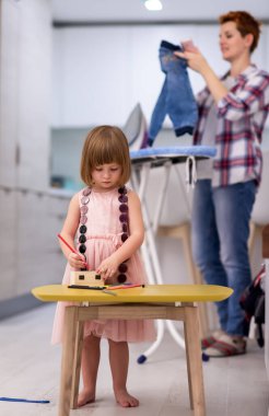 Mutlu bir aile, evde pembe elbiseli şirin bir kızla vakit geçirirken mücevher kutusunu boyar ve oynar. Bu arada genç kızıl saçlı anne de elbiselerini ütüler.