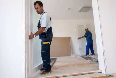 Erkek marangozlar, yeni lüks apartmana iç cam kapı döşüyorlar.