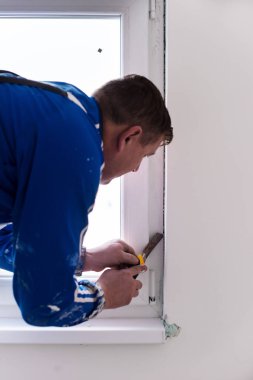 Genç profesyonel inşaat işçisi alçıtaşı duvarlara sıva yapıyor. Yeni, büyük, modern iki katlı apartmanın içinde.