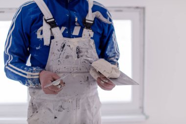 Genç profesyonel inşaat işçisi alçıtaşı duvarlara sıva yapıyor. Yeni, büyük, modern iki katlı apartmanın içinde.
