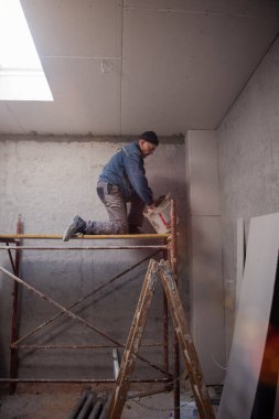 Genç profesyonel inşaat işçisi, alçı taşı tavanını sıva ile sıkarken yeni, modern iki katlı apartman dairesinde darağacını kullanıyor.